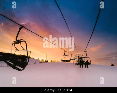 Orangefarbene und violette Wolken am Himmel als Sonnenuntergänge über dem Skilift im Winter Stockfoto