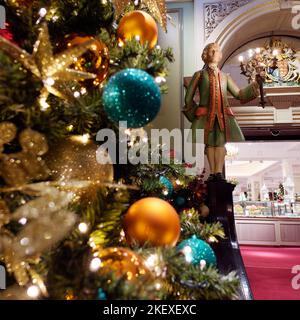 Dekorierter Weihnachtsbaum plus eine Statue eines Mannes mit einer Lampe am Eingang zum Fortnum and Mason Department Store in Piccadilly, London. Stockfoto