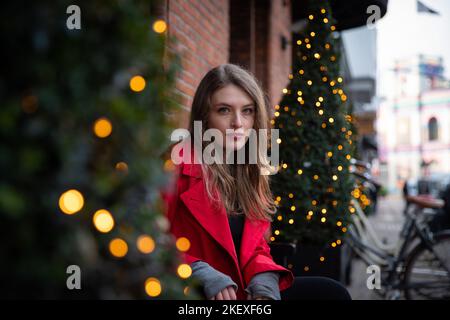 Mädchen sitzt auf einer Bank zwischen geschmückten Weihnachtsbäumen, Weihnachtszeit Stockfoto