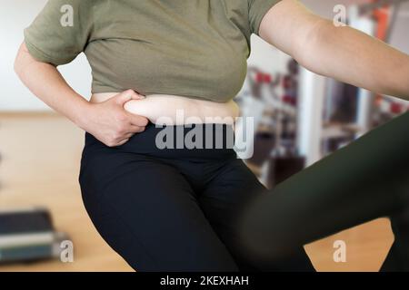 Aufnahme einer jungen Frau, die im Fitnessstudio auf einem Heimtrainer trainiert und ihre Fette kneifen soll Stockfoto