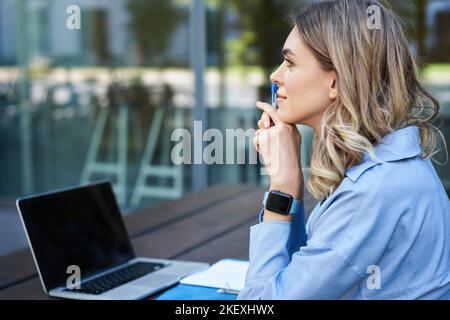 Nahaufnahme eines Porträts einer Studentin, die an Online-Kursen teilnimmt, mit einem Laptop an der frischen Luft sitzt und sich Notizen macht. Videochat für Geschäftsfrau Stockfoto