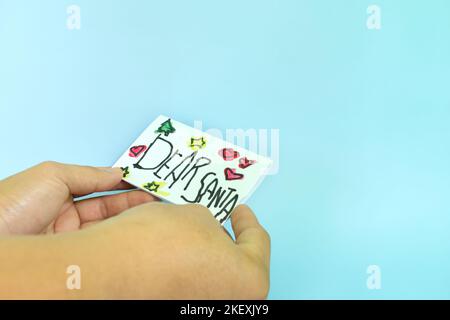 Weihnachtsbrief an den Weihnachtsmann vom Kinderkonzept. Nahaufnahme der menschlichen Hand mit einem Brief des lieben Weihnachtsmanns, der auf weißem Papier gezeichnet wurde. Stockfoto