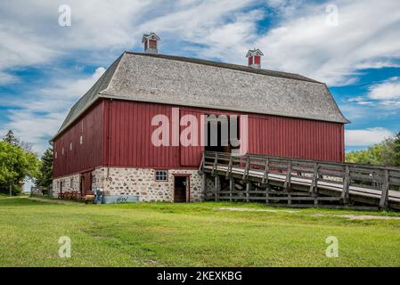 Abernethy, SK- 21. August 2022: Eine Frau in einem historischen Kostüm füttert ein Schaf vor W. R. Motherwells historischer Scheune aus dem Jahr 1907 auf seinem Gehöft Lanark Pl Stockfoto