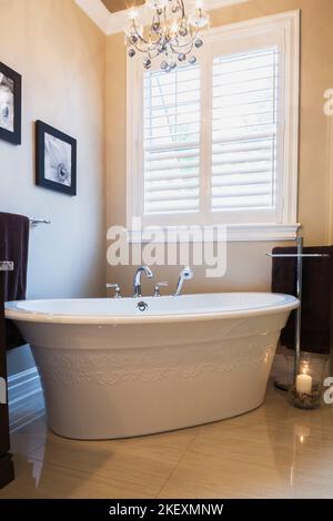 Weiße freistehende Badewanne mit geschnitzten dekorativen Details im Hauptbadezimmer im Erdgeschoss in einem modernen Landhausstil. Stockfoto