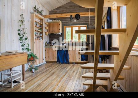 Einziehbare Kiefernholztreppen, klappbarer Esstisch und Küchenbereich mit 100 Jahre alten Ahornholzschränken in rustikalem 11,5 x 32 Fuß Mini-Haus. Stockfoto