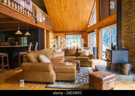 Braunes Ledersofa im Wohnzimmer mit Blick auf Küche und Mezzanin in einem gefrästen Cottage-Stil flaches Blockhaus. Stockfoto