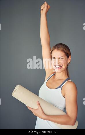 Jede Errungenschaft beginnt mit der Entscheidung zu versuchen. Eine Frau, die ihren Triumph ausdrückt, während sie ihre Yogamatte hält. Stockfoto