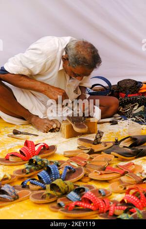 Pune, Indien - Nov 11 2022: Ein traditioneller Schuhmacher, der auf dem lokalen Markt traditionelle bunte Schuhe und Hausschuhe herstellt. Stockfoto