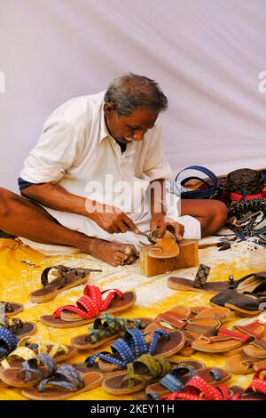 Pune, Indien - Nov 11 2022: Ein traditioneller Schuhmacher, der auf dem lokalen Markt traditionelle bunte Schuhe und Hausschuhe herstellt. Stockfoto
