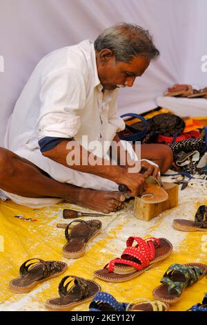 Pune, Indien - Nov 11 2022: Ein traditioneller Schuhmacher, der auf dem lokalen Markt traditionelle bunte Schuhe und Hausschuhe herstellt. Stockfoto