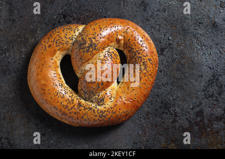 Frisch gebackene Brezeln mit Mohnsamen auf einem grüneisernen Hintergrund, Nahaufnahme, Draufsicht Stockfoto