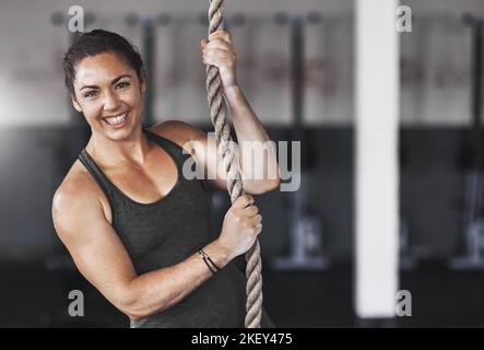 Ich bin bereit für den Aufstieg. Beschnittenes Porträt einer jungen Frau, die im Fitnessstudio ein Seil klettert. Stockfoto