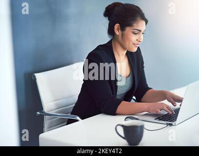 Eine attraktive junge Geschäftsfrau, die in ihrem Büro an einem Laptop arbeitet. Stockfoto