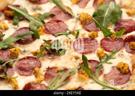 Heiße traditionelle italienische Pizza mit Salami, Fleisch, Käse, Tomaten und grünem Gemüse auf dunklem Hintergrund. Makro Stockfoto