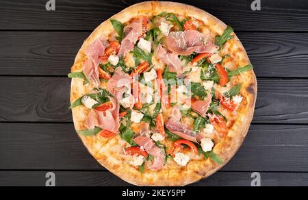 Pizza mit Schinken-Rucola und Parmesan auf dunklem Holzhintergrund von oben. Italienische Küche. Stockfoto