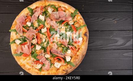 Pizza mit Schinken-Rucola und Parmesan auf dunklem Holzhintergrund von oben. Italienische Küche. Banner. Stockfoto