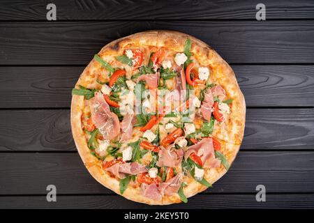 Pizza mit Parmaschinken, Mozzarella-Käse, Rucola, Kirschtomaten auf dunklem Hintergrund. Traditionelle italienische Pizza auf Holz Blick von oben Stockfoto