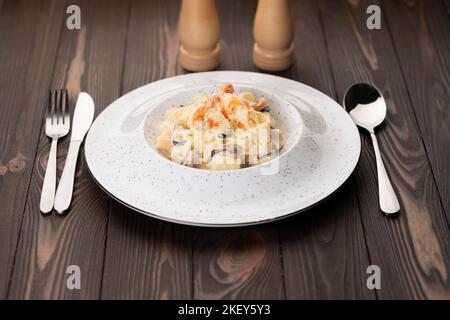Italienische Pasta Fettuccine mit Garnelen und Muscheln in cremiger Sauce mit Parmesan auf einem Teller, während sie auf dem Holztisch des Restaurants serviert wird. Stockfoto