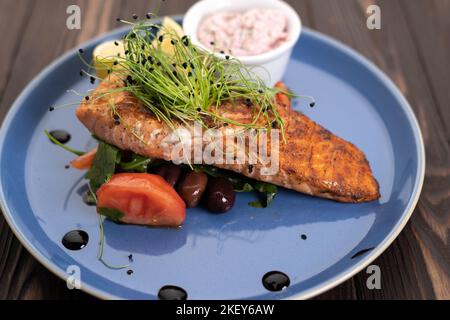 Gegrilltes Lachsfilet mit Tomaten und Zitrone auf einem blauen Teller auf einem Holztisch Stockfoto