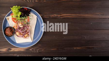 Kebab mit Soße und Gemüse auf einem Teller auf einem Holzhintergrund, Draufsicht Stockfoto