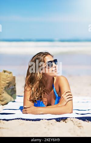 Eine schöne junge Frau, die am Strand auf einem Handtuch liegt. Stockfoto