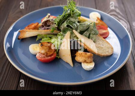 Frischer Caesar-Salat auf blauer Schüssel mit Parmesankäse und Garnelen. Stockfoto