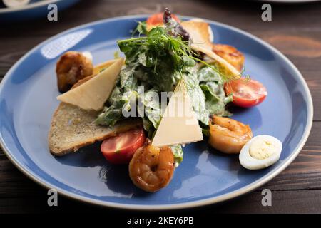 Frischer Caesar-Salat auf blauer Schüssel mit Parmesankäse und Garnelen. Stockfoto