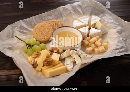 Käseplatte mit Honig, Trauben und Nüssen auf Holztisch Stockfoto