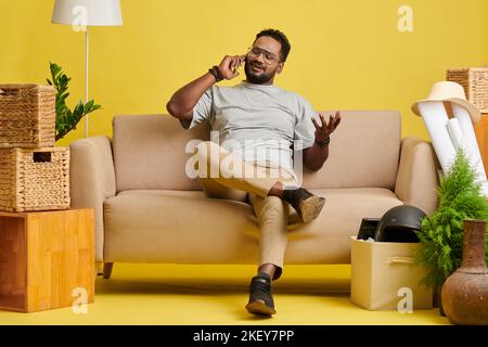 Glücklicher Mann, der sich auf dem Sofa entspannt hat, nachdem er hereinkam und telefoniert hatte Stockfoto