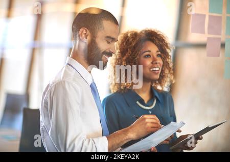 Unternehmer tun, was sie am besten können. Zwei junge Profis Brainstorming mit Haftnotizen an einer Glaswand in einem Büro. Stockfoto