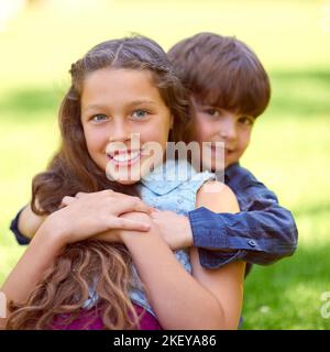 Meine kleinen Brüder haben mir immer den Rücken gekehrt. Porträt eines Jungen, der seine Schwester umarmt, während er draußen auf dem Gras sitzt. Stockfoto