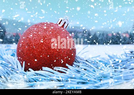 Rot glänzende Weihnachtskugel auf Tannenzweigen, mit verschwommenem Hintergrund und fallendem Schnee. Weihnachten, Neujahr. Speicherplatz kopieren Stockfoto