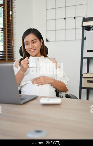 Portrait, schöne und professionelle asiatische schwanger Geschäftsfrau nippen Tee während der Arbeit in ihrem Büro. Geschäfts- und Schwangerschaftskonzept Stockfoto