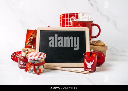 Weihnachtsgeschenk Mockup Web-Banner. Weihnachtsgeschenk für alle. Leeres schwarzes Brett und rot-brauner Zero Waste Becher, Einkaufstasche, Socken, Notizblock Stockfoto