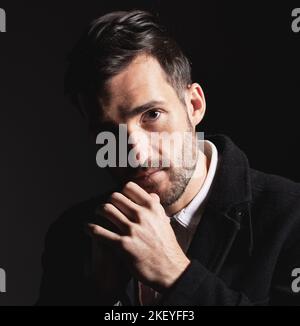 Porträt, Gesicht und Denken mit einem Mann Modell im Studio auf einem dunklen Hintergrund für Mode oder Stil. Idee, Hand und selbstbewusst mit einem hübschen jungen Mann Stockfoto