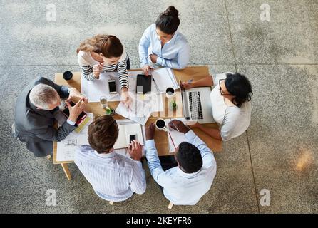 Ihre Ideen zusammenbringen. Aufnahme einer Gruppe von Geschäftsleuten, die an einem Tisch sitzen und arbeiten. Stockfoto