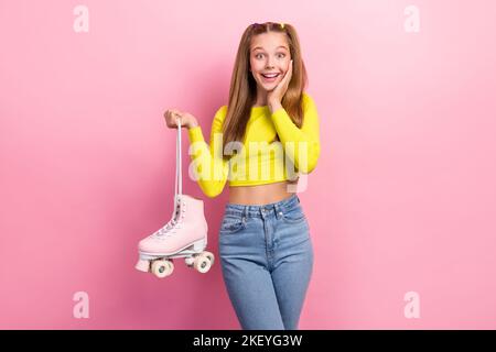 Foto von funky beeindruckt Schulmädchen gekleidet gelb Ernte oben Arme Wange steigenden Retro-Rollen isoliert rosa Farbe Hintergrund Stockfoto