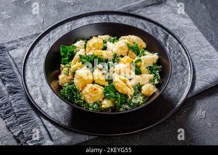Eine Portion kitschig gebackene Muschelpasta mit grünem Blattkohl und knusprigen Paniermehl in einer schwarzen Schüssel auf einem Betontisch Stockfoto