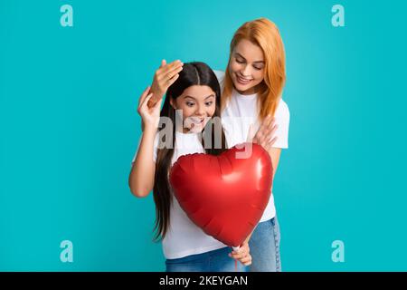 Muttertag. Lächelnde Mutter und Tochter halten den Liebesherz-Ballon auf blauem Hintergrund. Glücklicher Muttertag für meine Mutter. Stockfoto