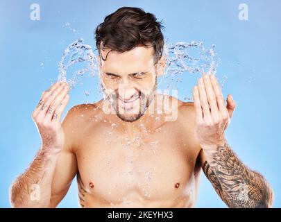 Pflege, Spritzer und Mann waschen Gesicht mit Wasser für Reinigung, Hygiene und Wellness vor einem blauen Studio Hintergrund. Hautpflege, Schönheit und Modell mit Stockfoto