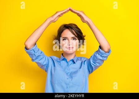 Portrait Foto von jungen attraktiven netten netten Frau bob braune Haare Mädchen demonstriert ihr neues Haus Sicherheit Hände Symbol isoliert auf gelbe Farbe Stockfoto