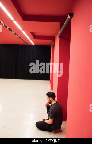 Junger nachdenklicher bärtiger Mann, der im roten Raum auf dem Boden sitzt Stockfoto