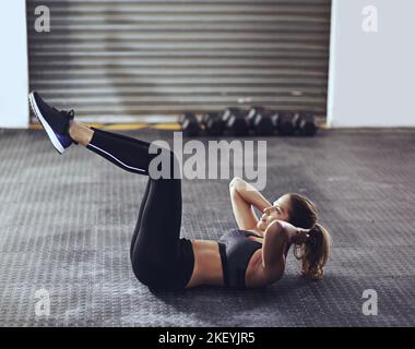 Holen Sie sich Ihre Kernkraft in Schach. Eine junge Frau, die Sit-ups im Fitnessstudio macht. Stockfoto