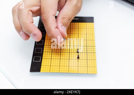 Eine Männerhand legt eine kleine Schraube auf eine gelbe Magnetmatte Nahaufnahme. Computer und Telefon reparieren Stockfoto