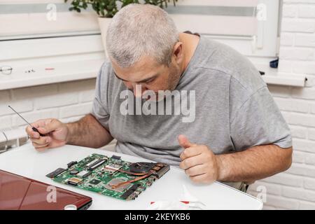 Nahaufnahme eines Mannes, der einen Laptop mit einem Schraubendreher und verschiedenen Werkzeugen auf dem Tisch fixiert Stockfoto