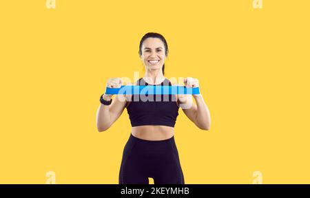 Sportlerin auf gelbem Hintergrund mit ihren Händen dehnt Gummiband für das Training. Stockfoto