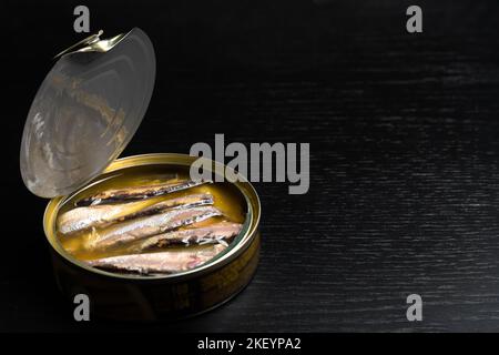 Nahaufnahme einer offenen Dose Sprotte in Öl auf schwarzem Hintergrund, Platz kopieren. Stockfoto