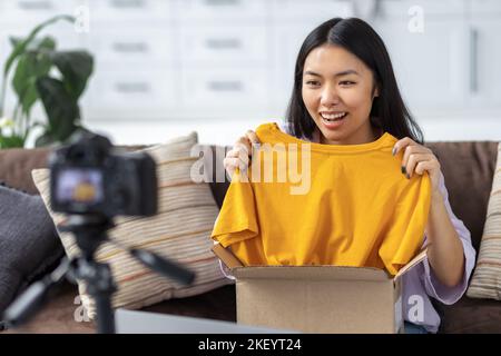Glückliche Frau Freiberufler Auspacken Box von Kleidung vor der Kamera Junge asiatische Freiberuflerin Bloggerin Stockfoto