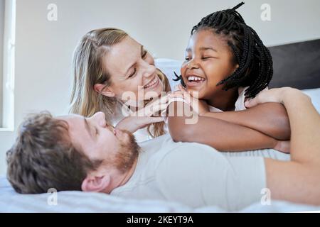Entspannen, Adoption und Vielfalt mit Familie im Schlafzimmer für glücklich, Unterstützung und Bindung am Morgen. Aufwachen, lächeln und mit Pflegekind spielen Stockfoto