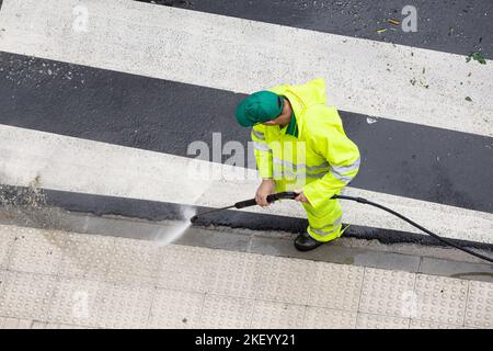 Arbeiter putzen einen Straßensteig mit Hochdruckwasserstrahl. Öffentliche Instandhaltung Stockfoto